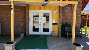 A building entrance with a yellow awning, a door marked 'OFFICE', and a bench outside.