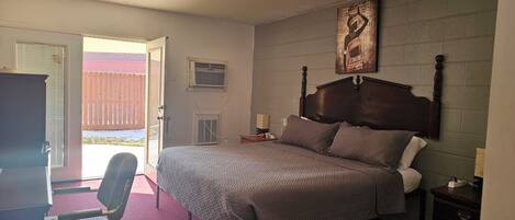 A bedroom with a bed, two bedside tables, a chair, and an open door leading to a balcony.