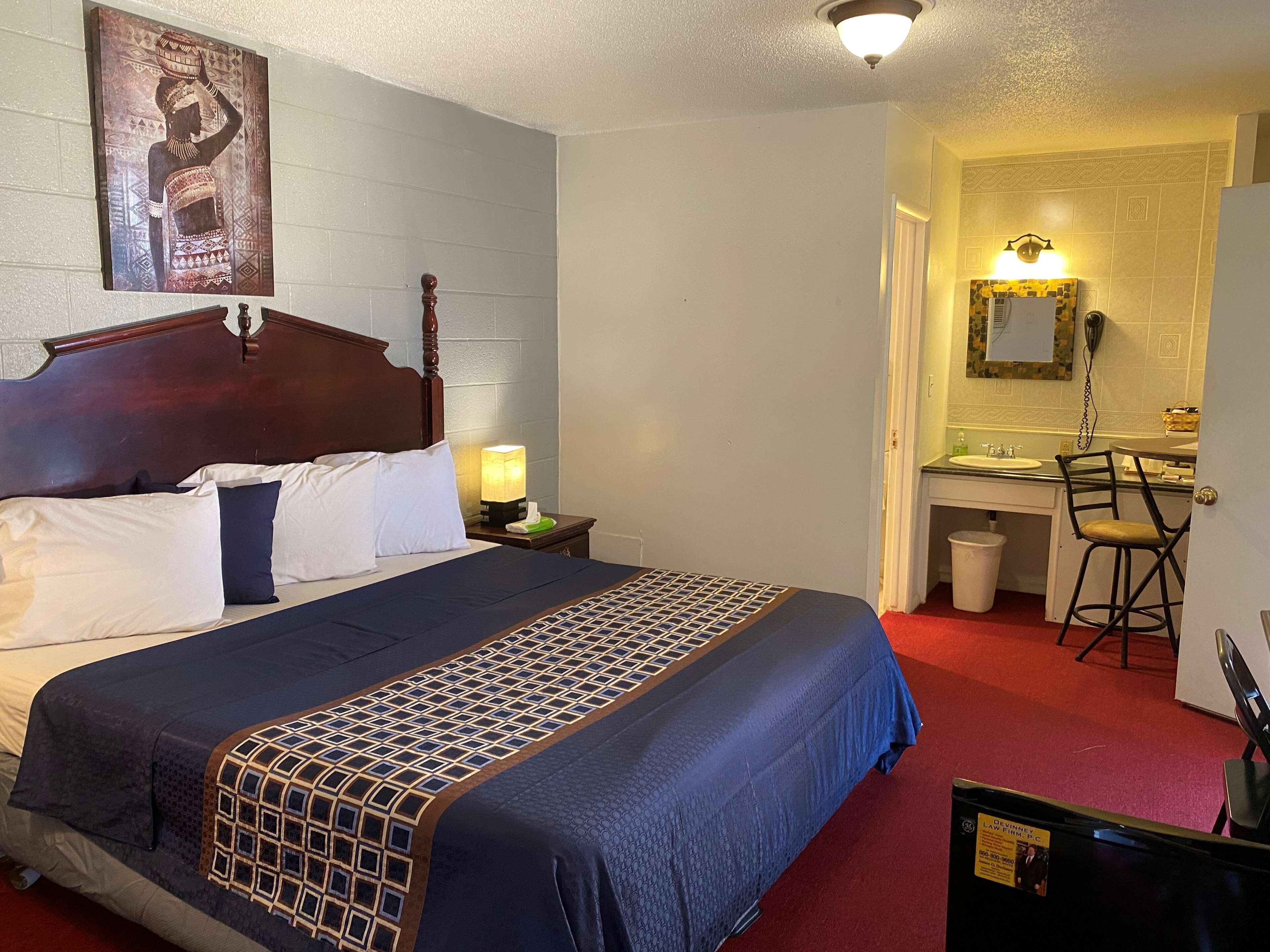 A hotel room with a bed, a desk, a chair, a nightstand, and a bathroom visible through an open door.