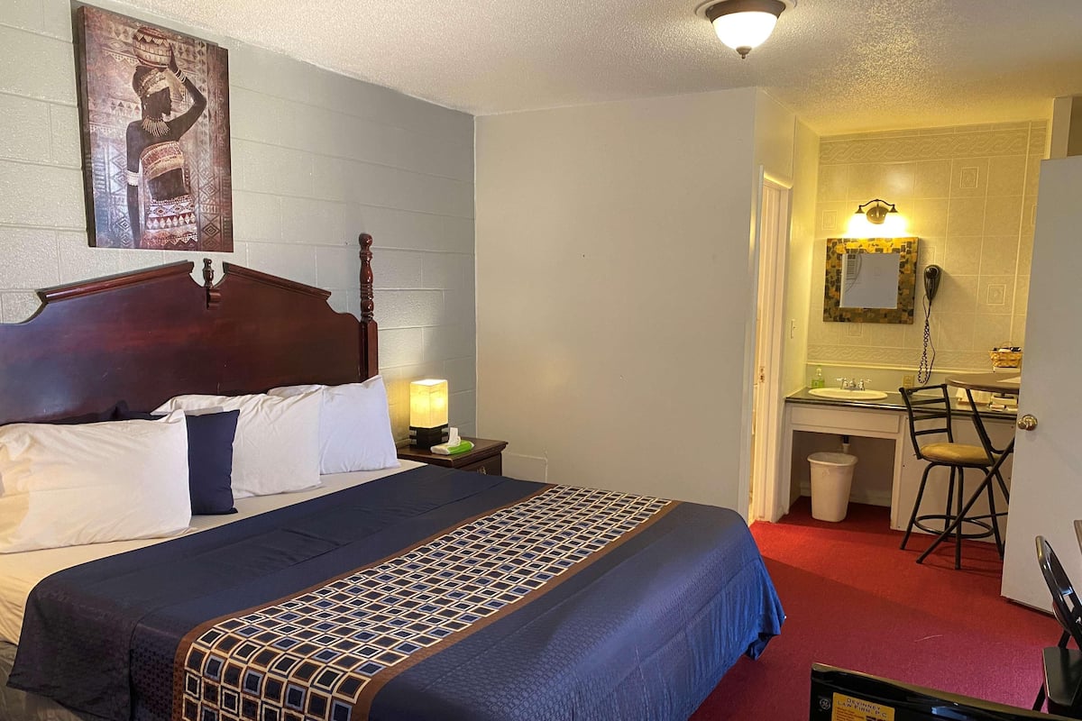 A hotel room with a bed, a desk, a chair, a nightstand, and a bathroom visible through an open door.