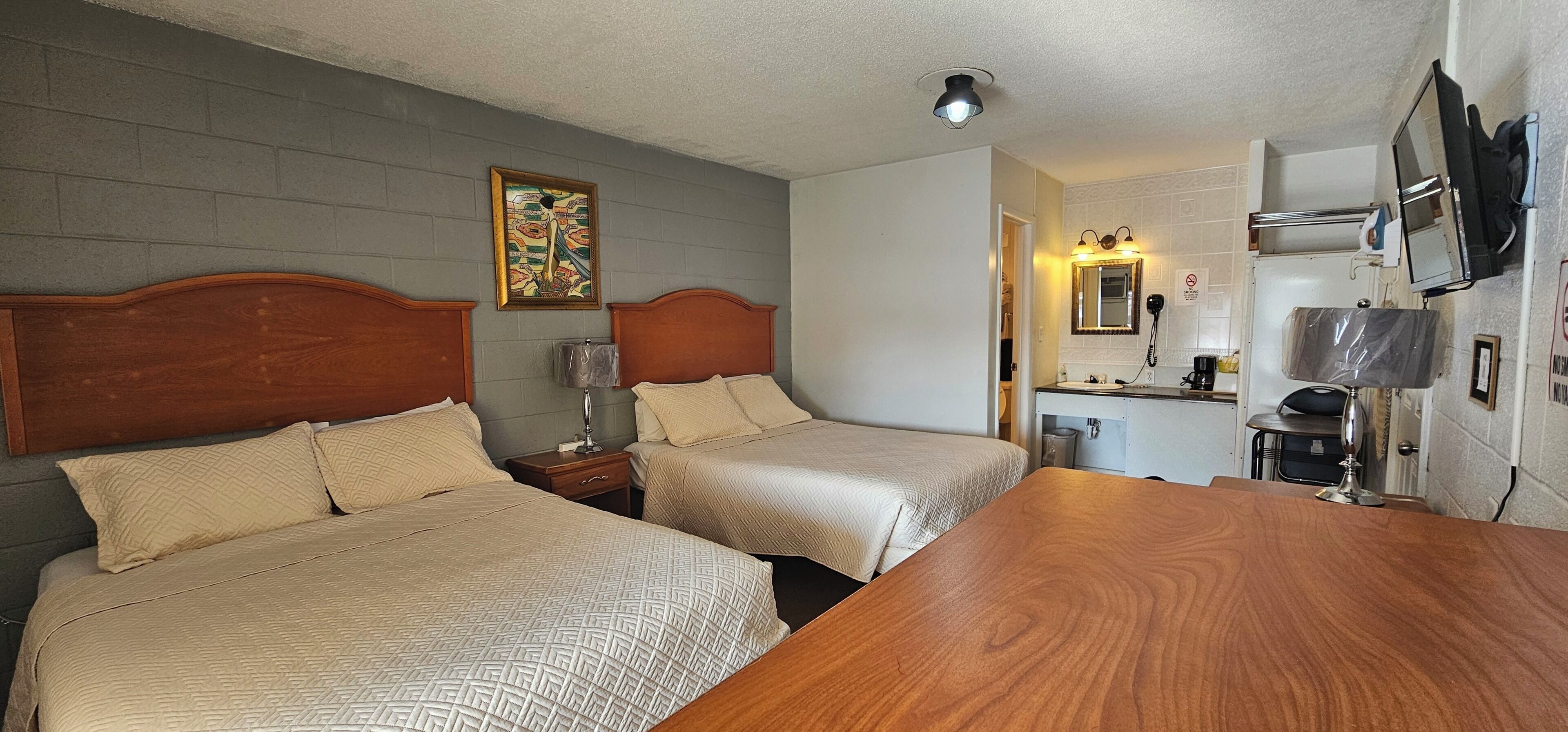 A hotel room with two beds, a wooden table, a small desk, a television, and a bathroom visible through an open door.