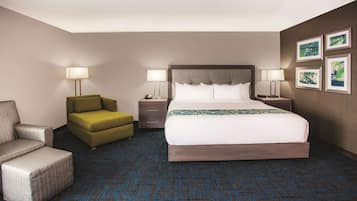 Ein Hotelzimmer mit einem großen Bett, zwei Nachttischen, einem grünen Sessel und einem grauen Sessel, sowie einem gemusterten Teppich.