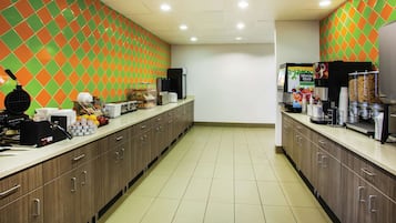 Un coin cuisine avec un mur recouvert de carreaux, un appareil à gaufres, des machines à café et un distributeur de boissons.