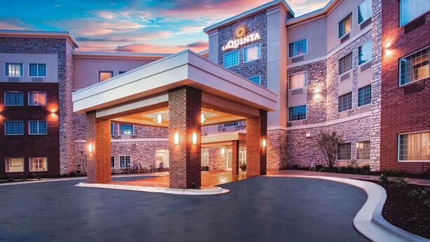 Entrada de hotel con vestíbulo cubierto, varios pisos y un llamativo letrero de 'La Quinta'.
