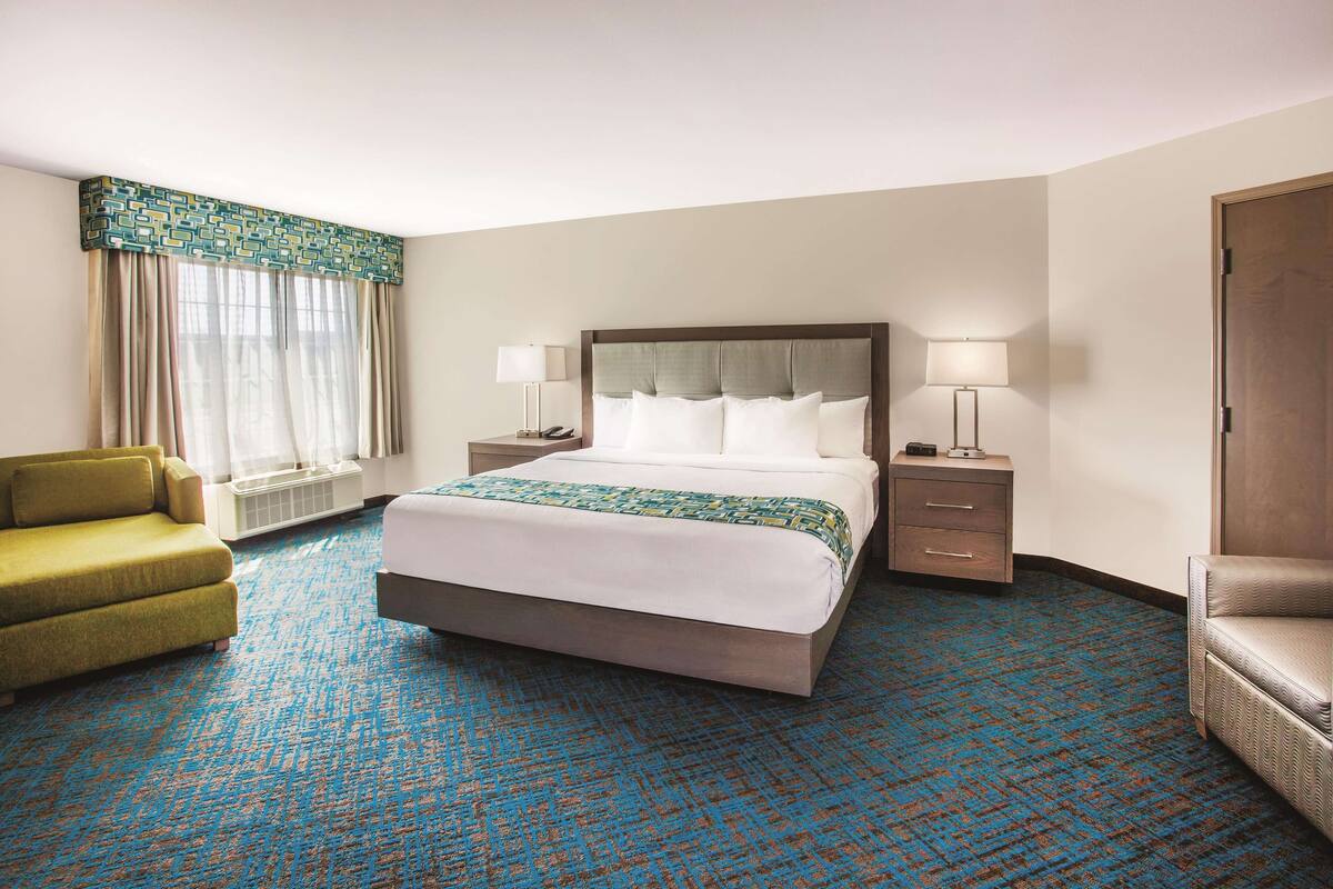 A hotel room with a large bed, two bedside tables with lamps, a green armchair, and a patterned carpet.