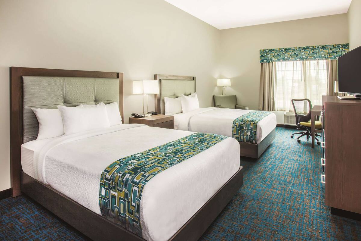 A hotel room with two beds, a desk, a chair, and a television.