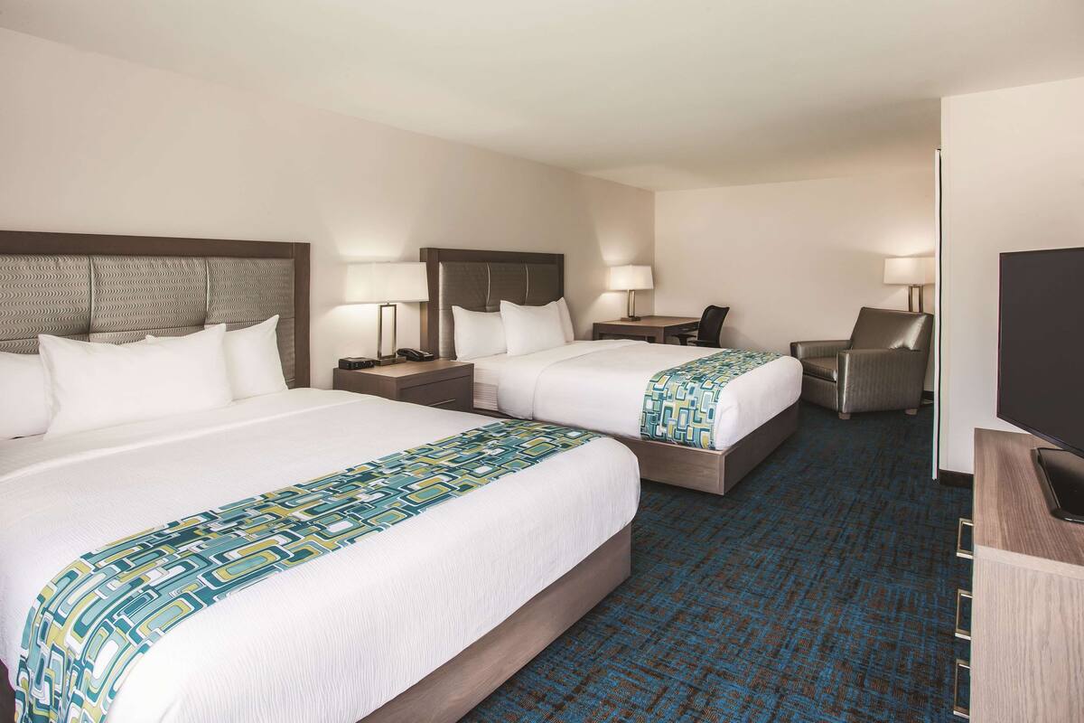 A hotel room with two beds, a desk, a chair, and a TV.