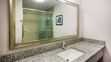 Casa de banho com bancada de granito, lavatório, espelho e porta de chuveiro em vidro.