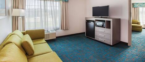 Une chambre d’hôtel équipée d’un canapé, d’une télévision, d’un four à micro-ondes et d’une petite kitchenette.