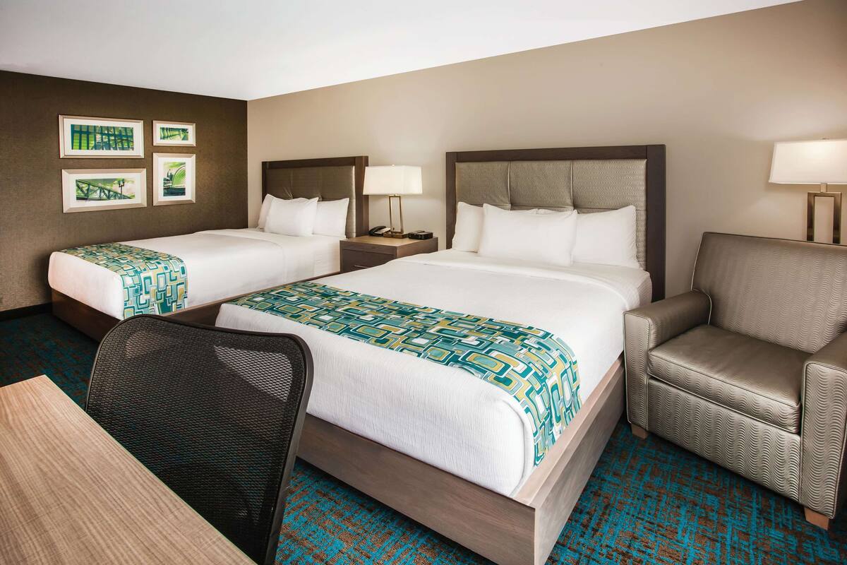 A hotel room with two beds, a desk, and a chair.