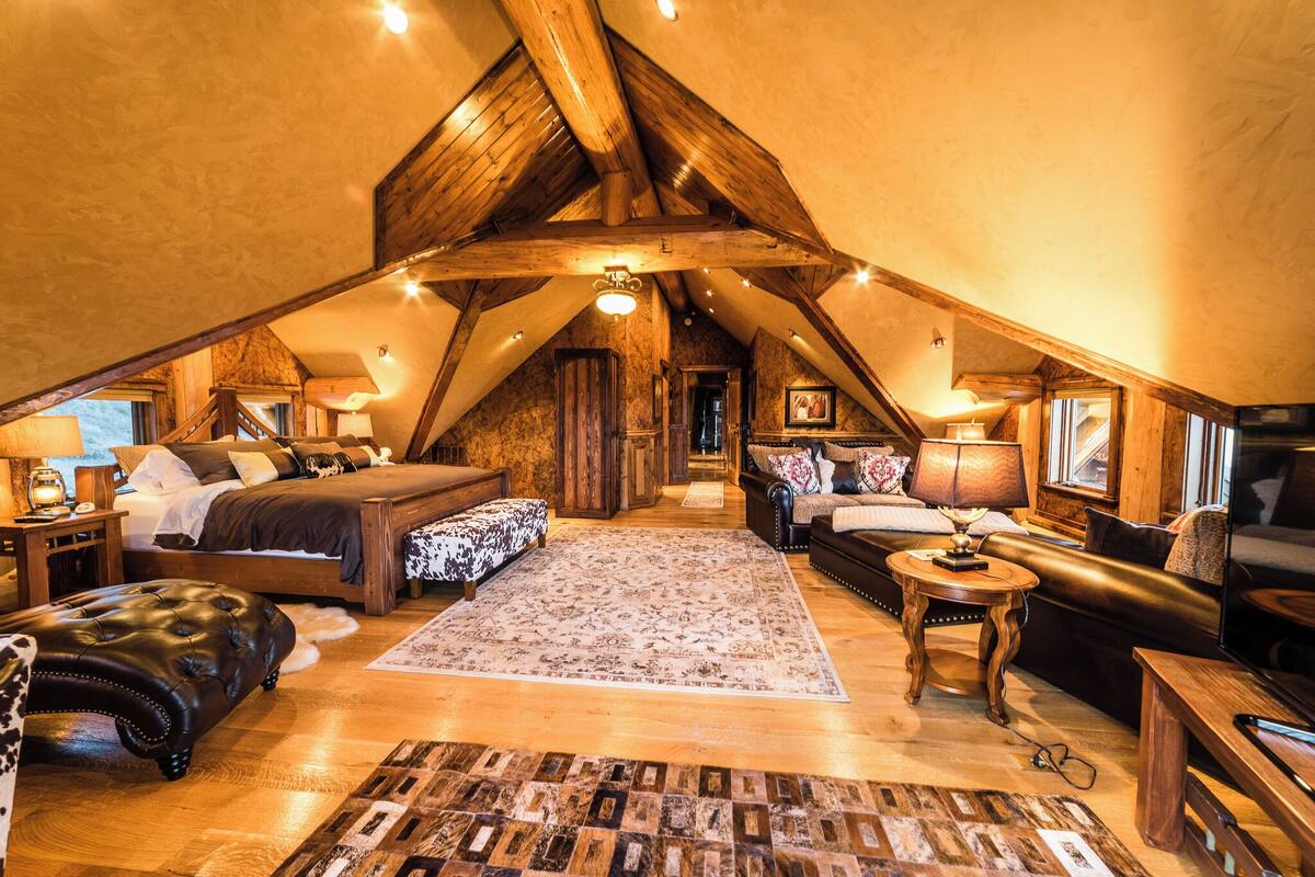 An attic bedroom with a loft bed, a sofa, a coffee table, and a TV.