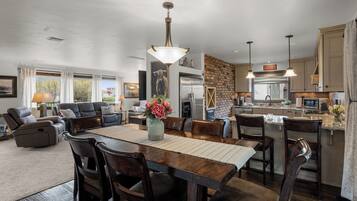 A spacious living area with a dining table, comfortable seating, a kitchen with modern appliances, and a large window offering a view of the outdoors.