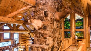 Um interior rústico com lareira de pedra, vigas de madeira e chifres de veado fixados na parede.