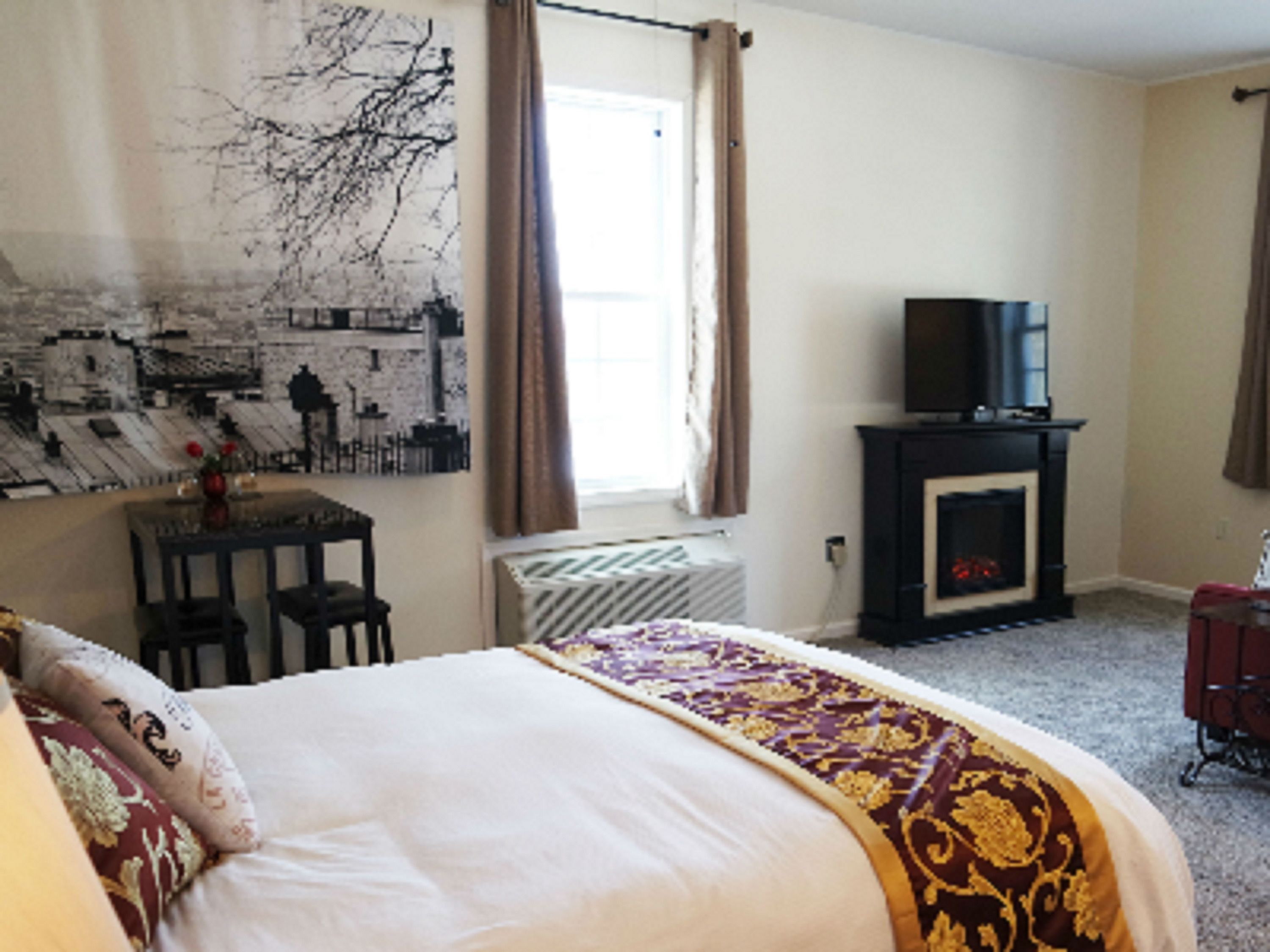 Une chambre à coucher avec un lit, un téléviseur posé sur un meuble, une cheminée et une fenêtre avec des rideaux.