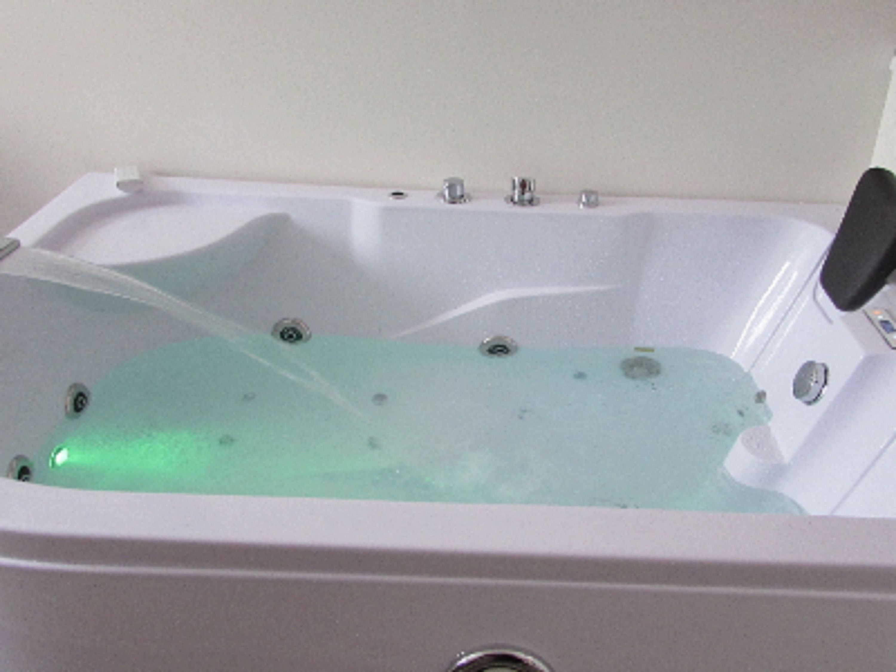Una bañera blanca con una fuente de agua verdosa, un grifo negro y un desagüe visible.