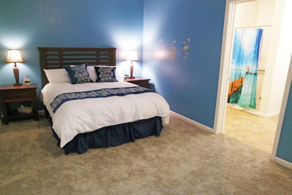 Une chambre à coucher avec un lit, deux tables de chevet avec des lampes, un mur bleu et une porte avec un rideau.