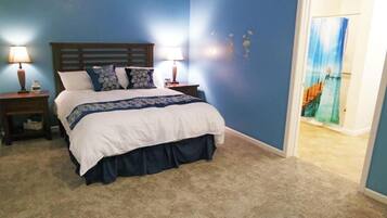 Une chambre à coucher avec un lit, deux tables de chevet avec des lampes, un mur bleu et une porte avec un rideau.