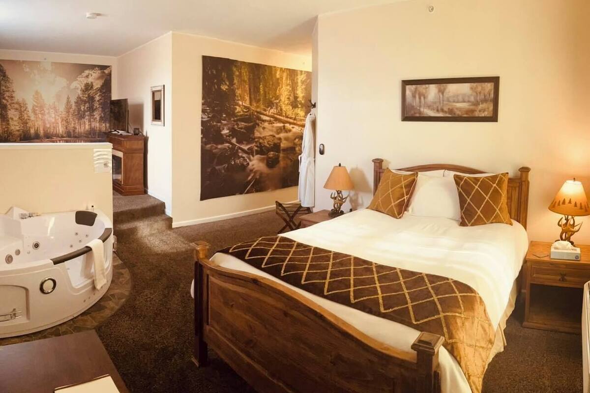 Une chambre d’hôtel avec un grand lit, un coin salon comprenant une chaise et une petite table, une baignoire et un tableau au mur.