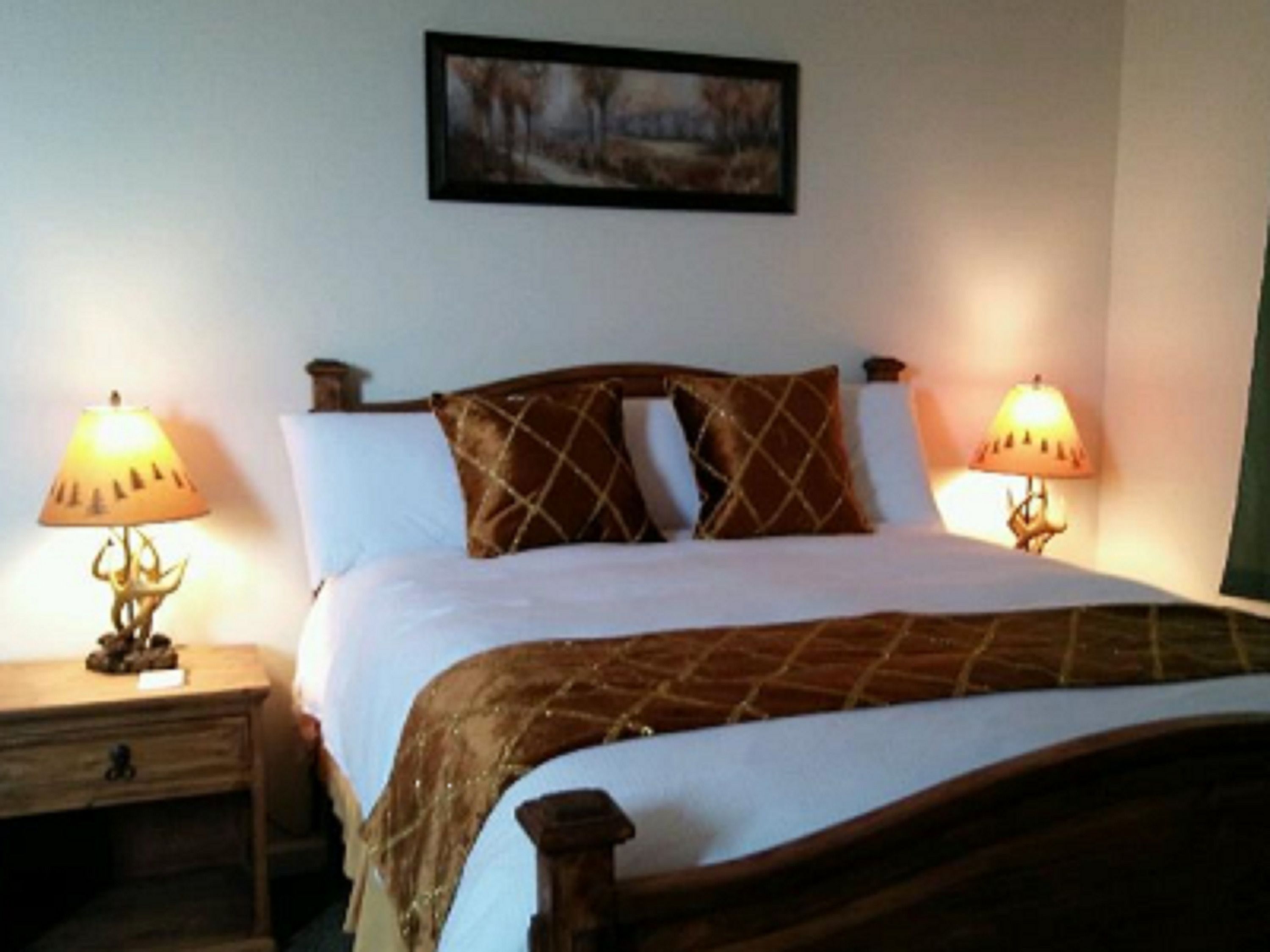 Un lit bien fait, recouvert d’une couvre-lit marron à motifs, avec deux lampes de chevet et un tableau encadré accroché au mur.