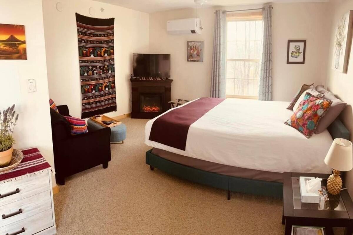 Une chambre à coucher avec un grand lit, une cheminée, une télévision et une fenêtre avec des rideaux.