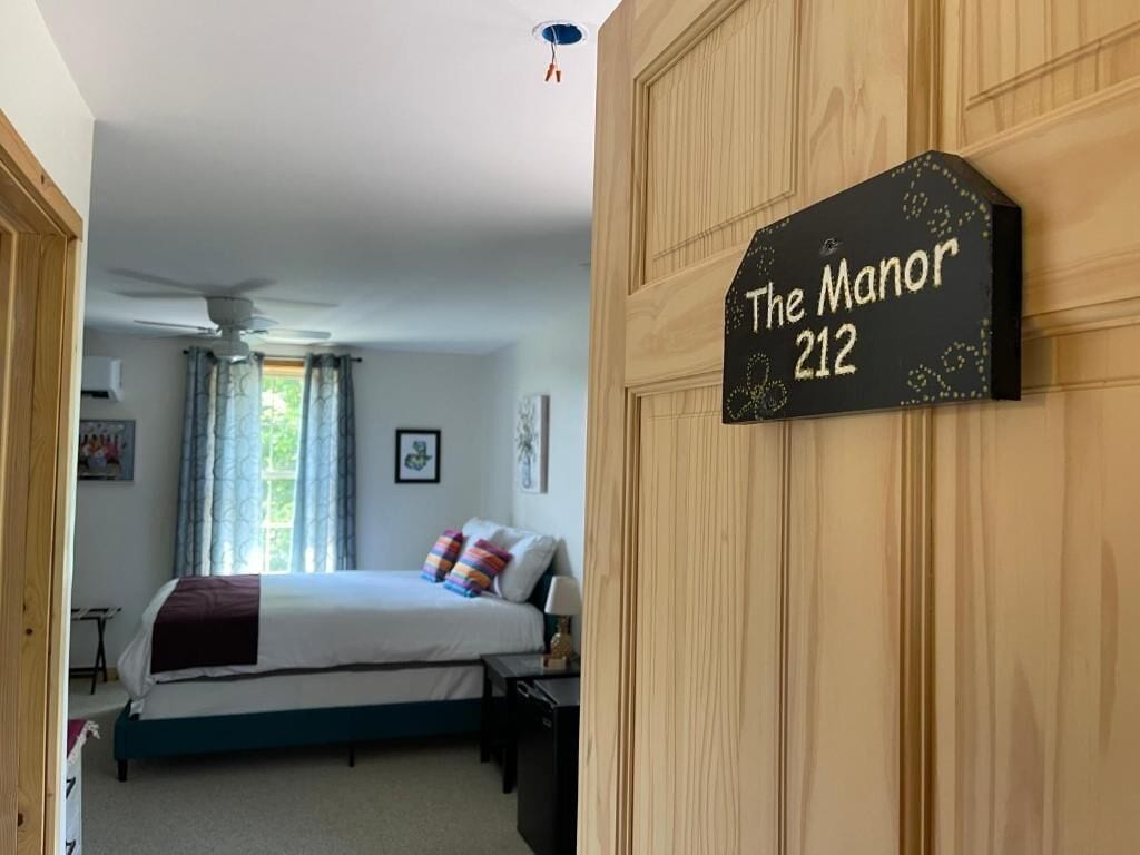 Un dormitorio con cama, mesita de noche y cómoda. Hay un cartel en la pared que dice 'The Manor 212'.