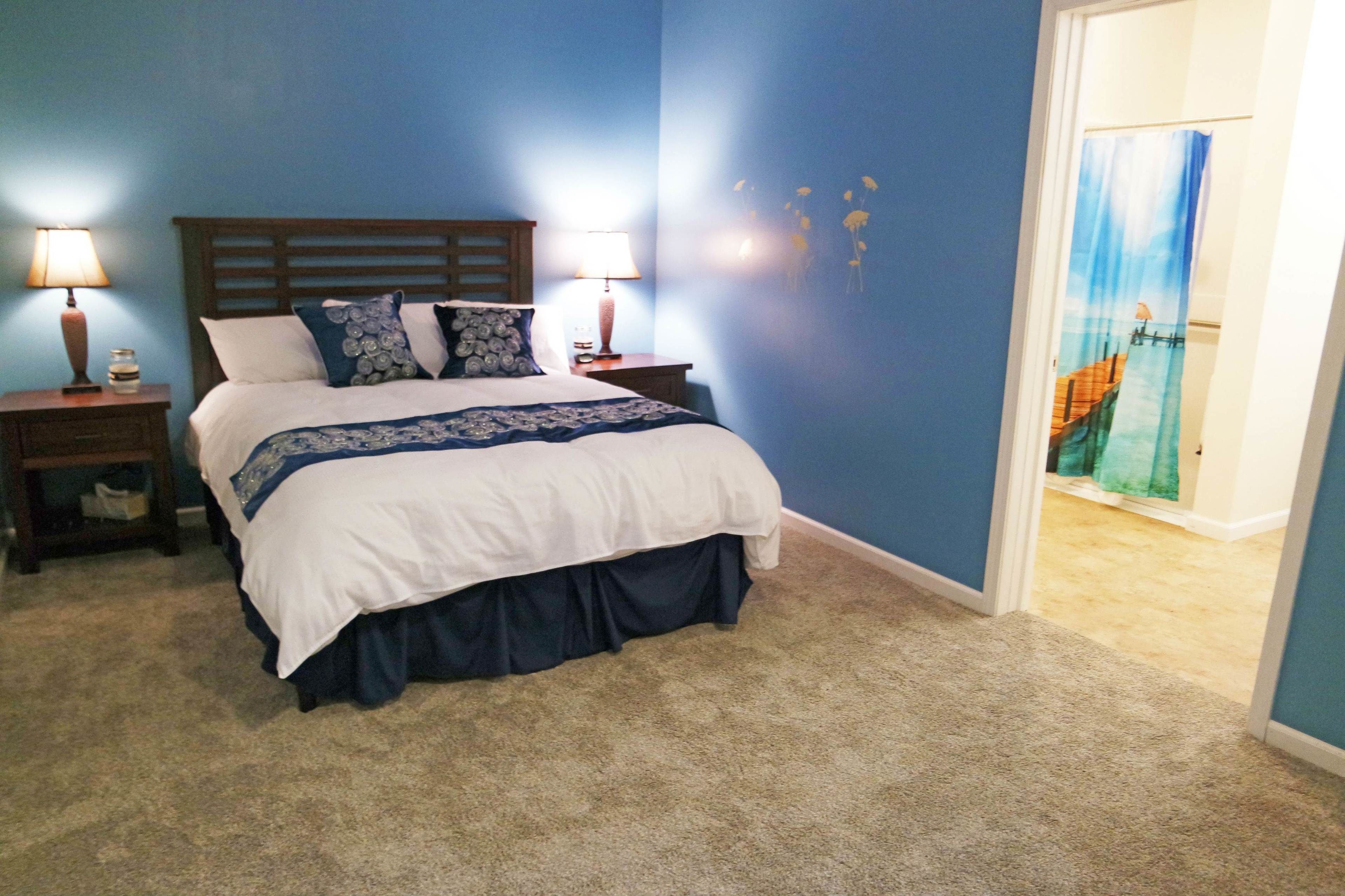 Une chambre à coucher avec un lit, deux tables de chevet avec des lampes, un mur bleu et une porte avec un rideau.