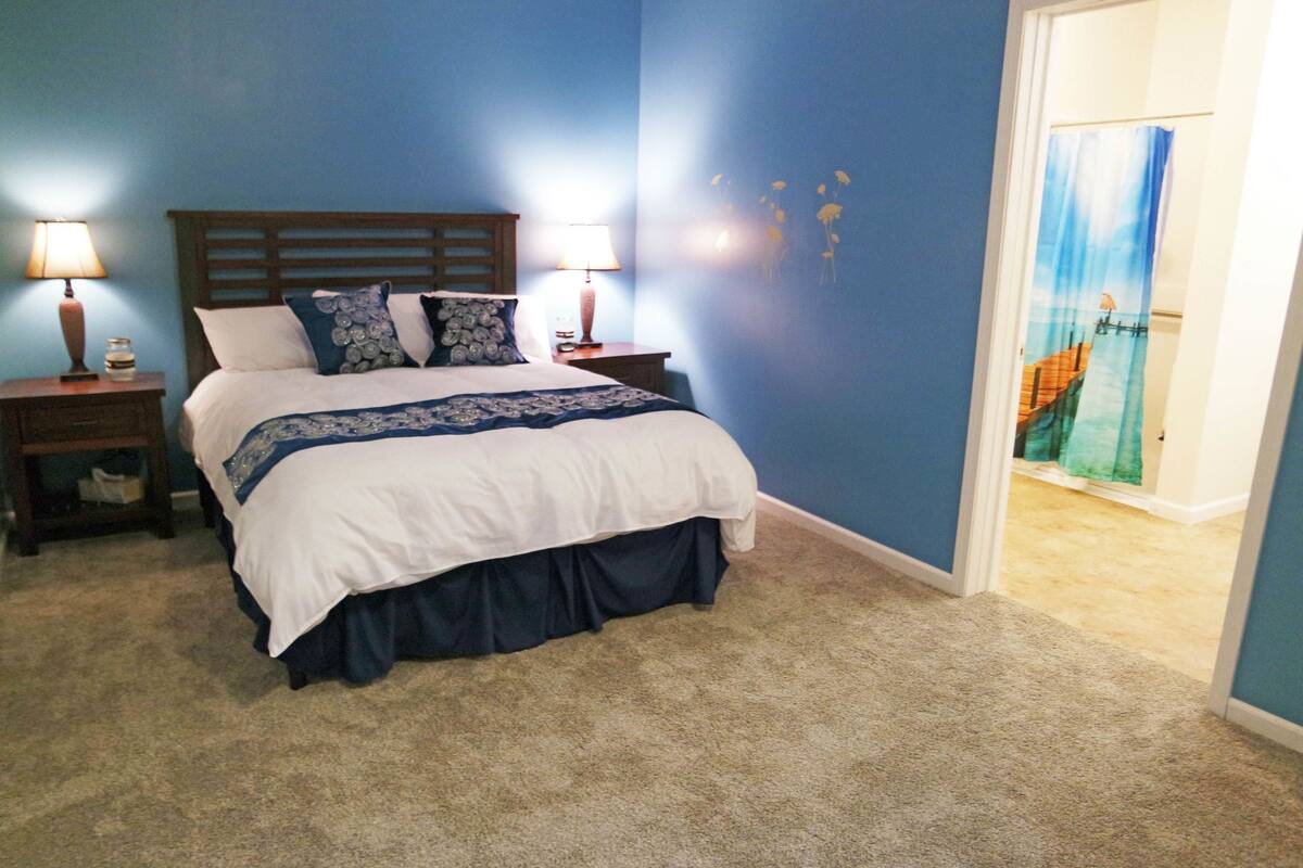 Une chambre à coucher avec un lit, deux tables de chevet avec des lampes, un mur bleu et une porte avec un rideau.