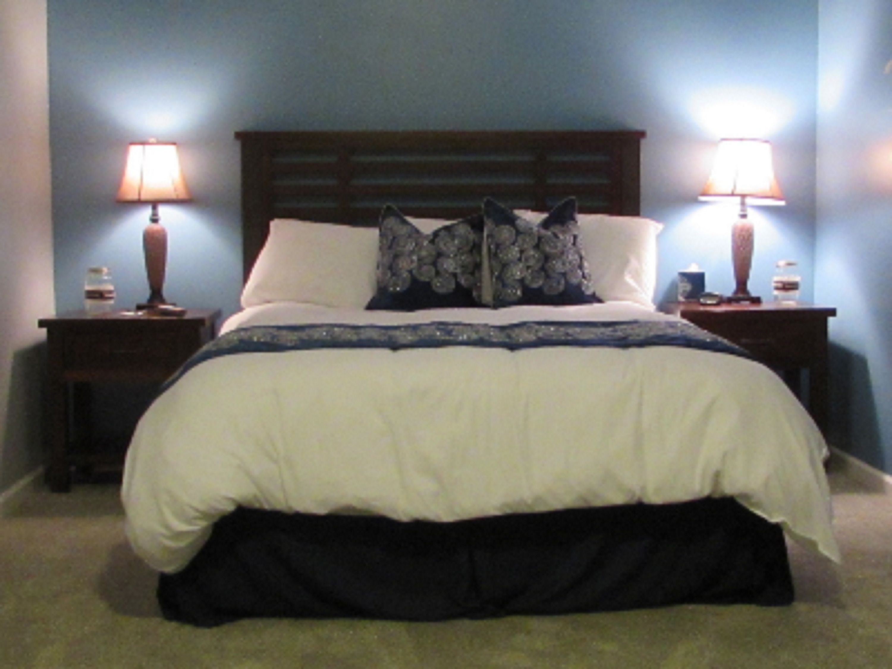 A neatly made bed with a wooden headboard, two bedside lamps, and a dark skirted bed skirt.