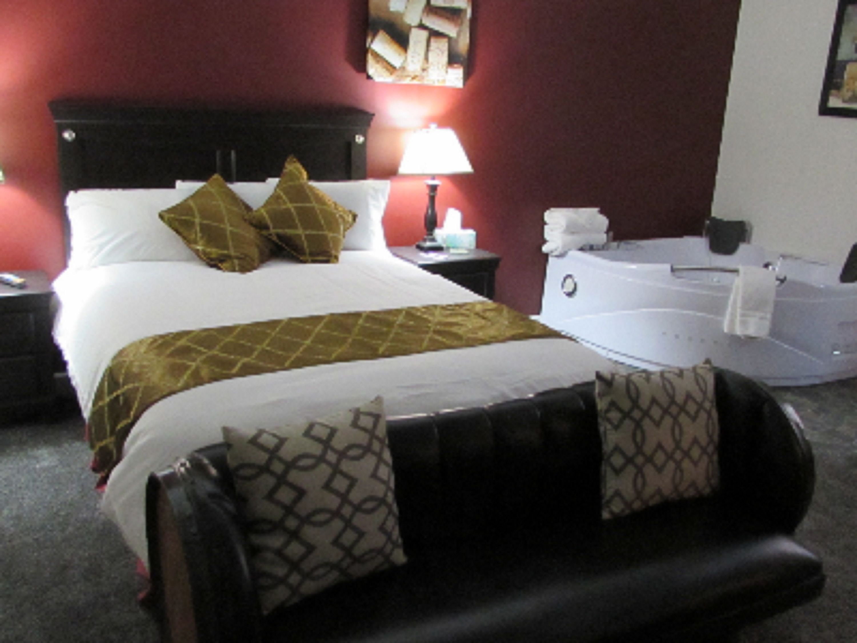 Une chambre d’hôtel avec un grand lit, une table de chevet, une lampe, une salle de bain avec une baignoire et un mur rouge.