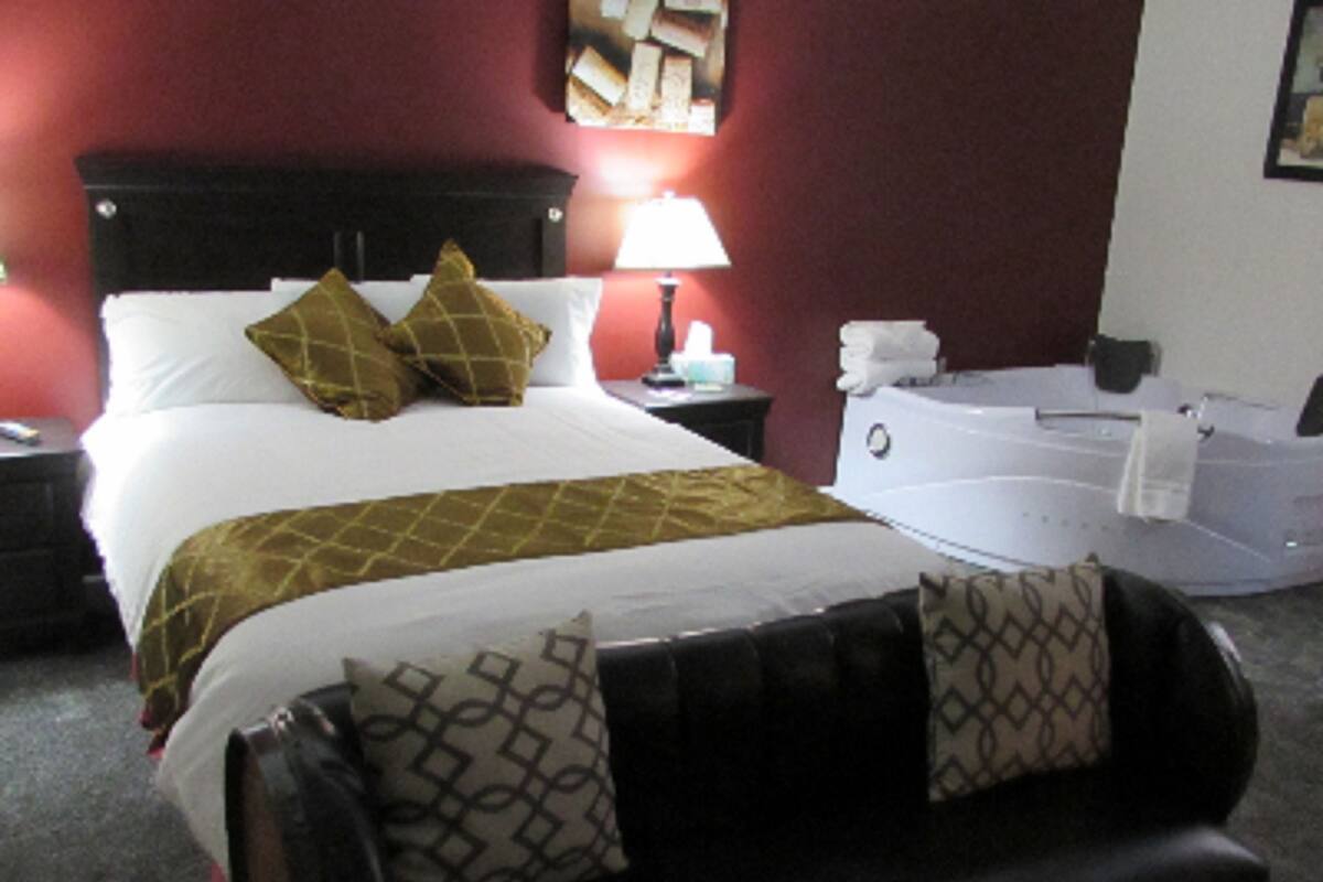Une chambre d’hôtel avec un grand lit, une table de chevet, une lampe, une salle de bain avec une baignoire et un mur rouge.