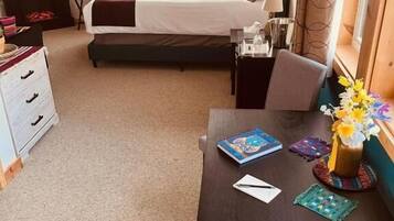 Quarto de hotel com cama, escrivaninha, cadeira, cômoda, televisão e janela com cortinas.