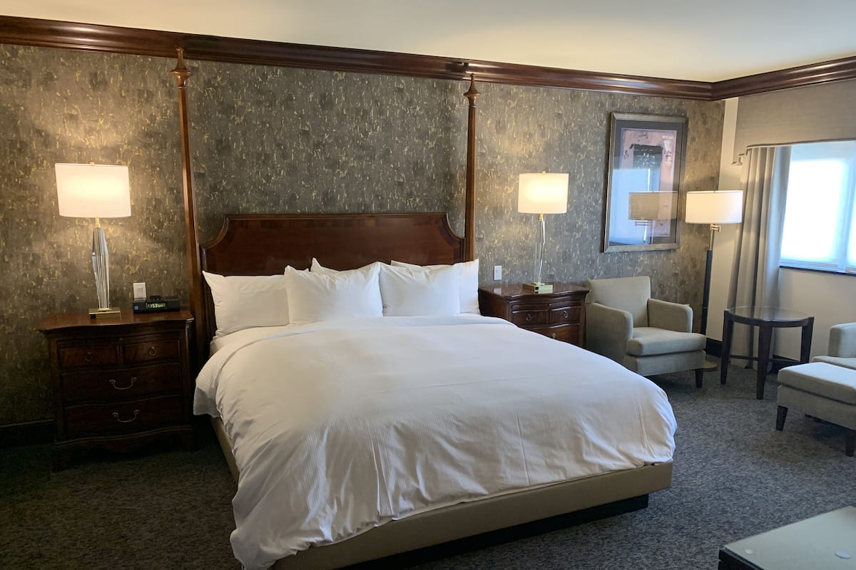 Una habitación de hotel con una cama grande, dos mesitas de noche, una silla, un escritorio y una lámpara.