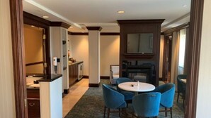Hotelkamer met een eethoek, bestaande uit een ronde tafel en blauwe stoelen, een kitchenette met een magnetron en kastjes, en een grote spiegel boven de wastafel.