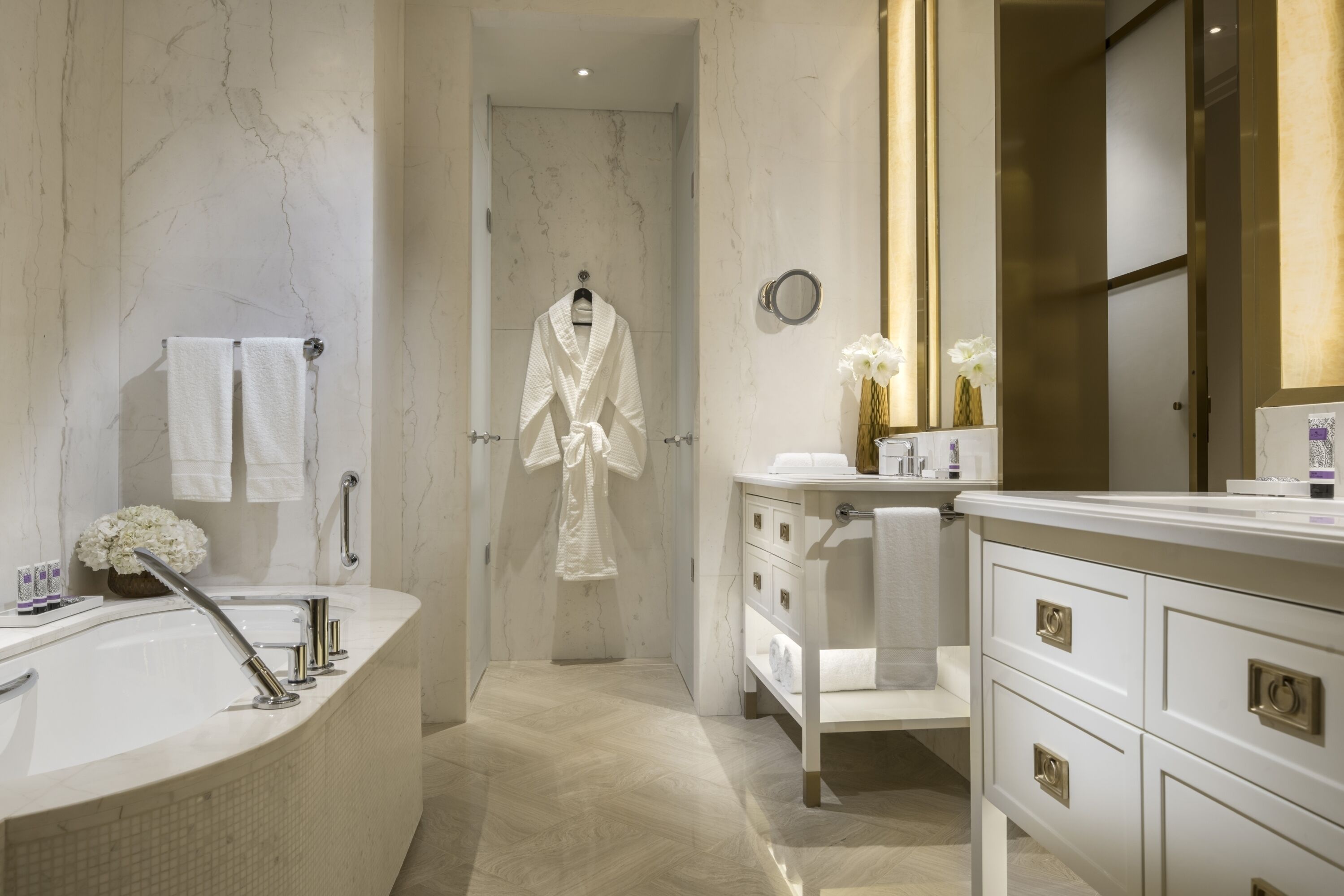 Un baño moderno con una bañera independiente, un tocador con espejo y una bata colgada en una puerta.