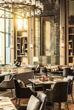 Un restaurante moderno con candelabro, mesas dispuestas para comer y una gran pared con textura.