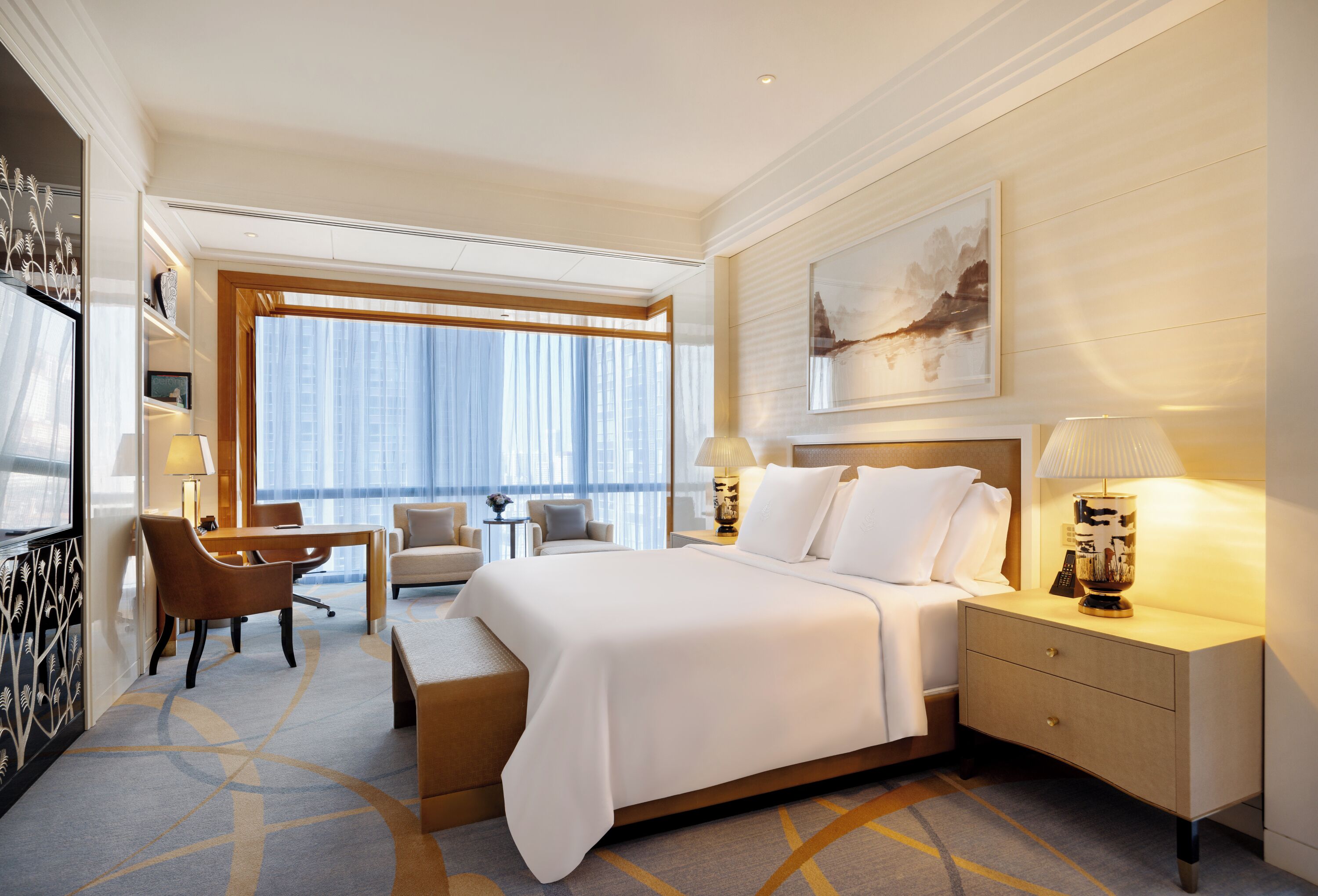 Quarto de hotel com uma cama grande, uma mesa, uma cadeira, uma mesa de cabeceira e uma janela ampla com cortinas.
