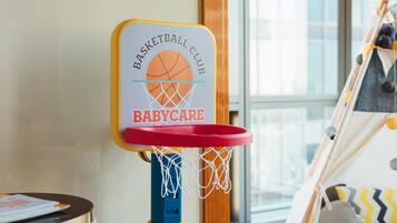 A basketball hoop with a sign reading "Basketball Club Babycare" in a room with a window and a tent-like structure in the background.