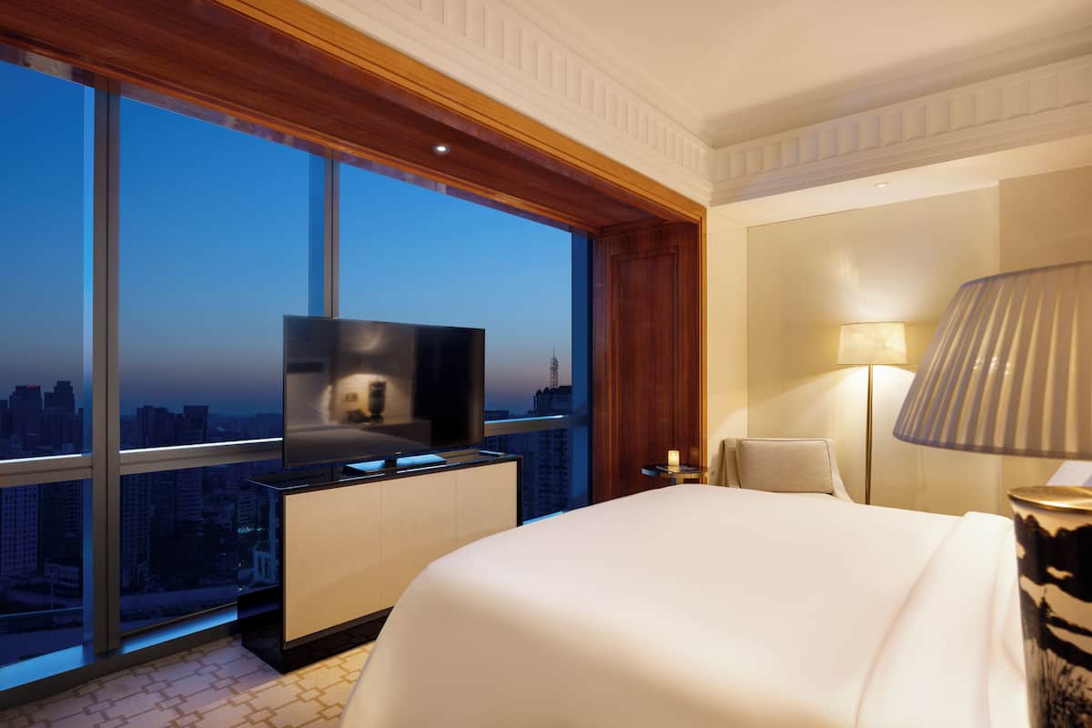 Habitación de hotel con un ventanal grande, una televisión de pantalla plana, una cama, una mesita de noche y una lámpara.