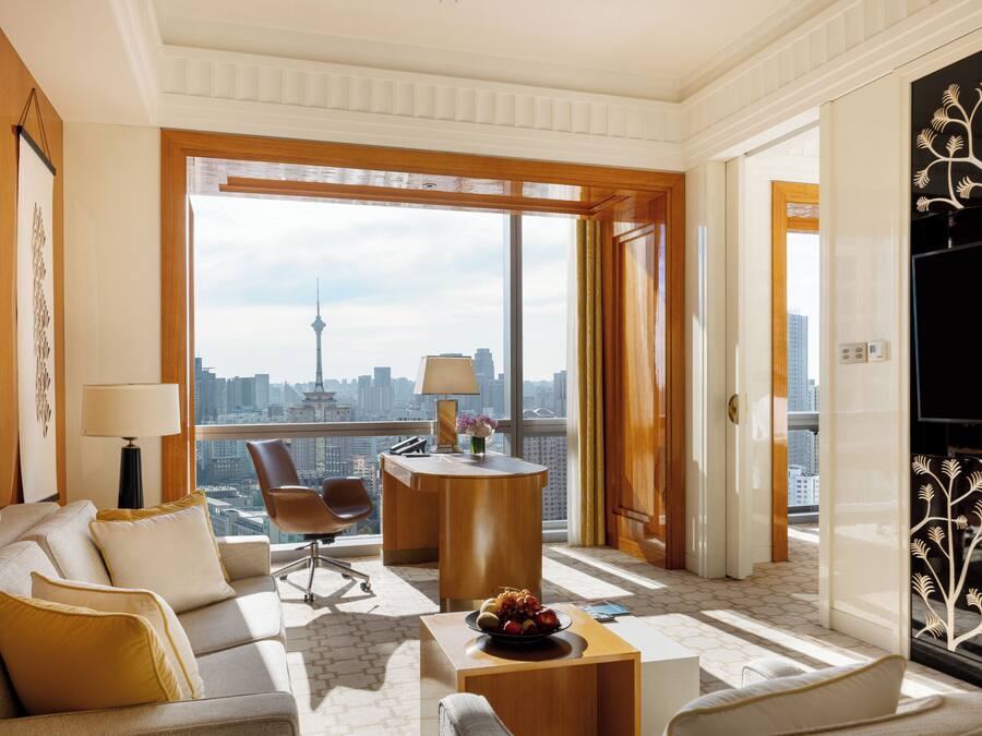 A spacious living room with a large window, a round coffee table, a sofa, and a TV.