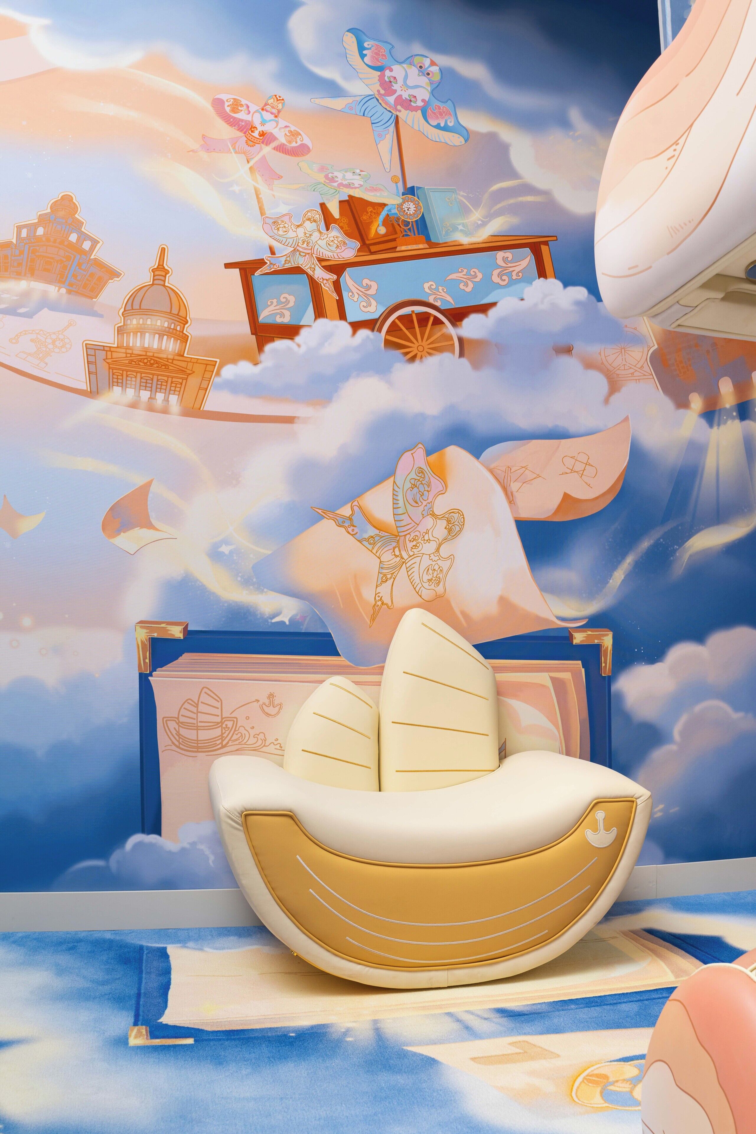 A room with a large mural of clouds, a ship, and a castle. There is a white boat-shaped chair and a blue suitcase on the floor.
