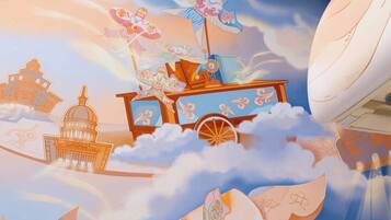 A room with a large mural of clouds, a ship, and a castle. There is a white boat-shaped chair and a blue suitcase on the floor.