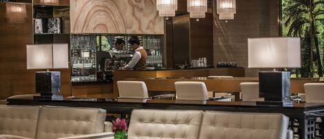 A modern bar area with a bartender, cushioned seating, and a large window with a view of palm trees.