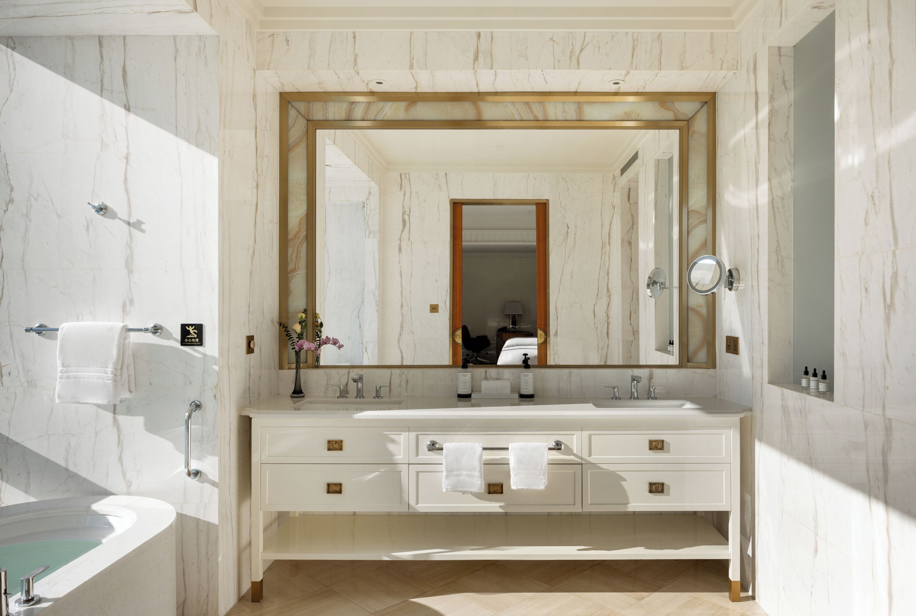 Un baño con un espejo grande, una bañera, un tocador con dos lavamanos y toallas colgadas en la pared.