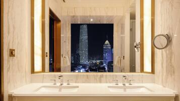 A modern bathroom with two sinks, a large mirror, and a view of a cityscape at night.