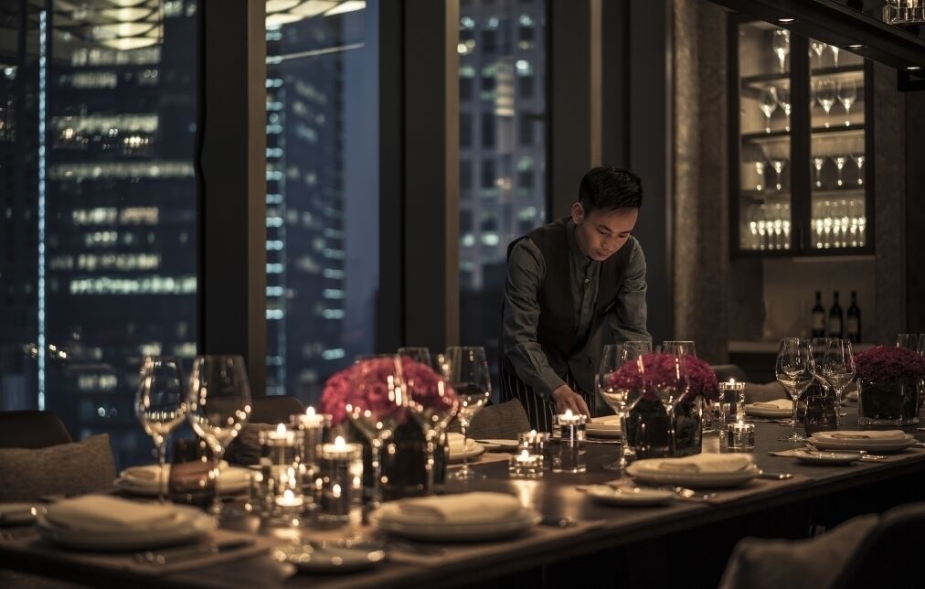A well-set dining table with candles, glasses, and a city view.