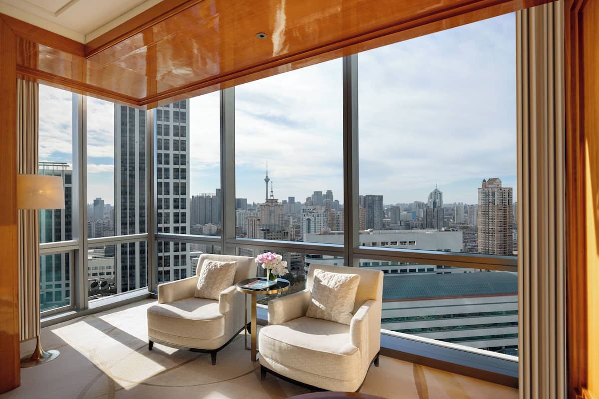 Habitación en un rascacielos con ventanas amplias, dos sillones, una mesita con un florero y vistas a la ciudad.