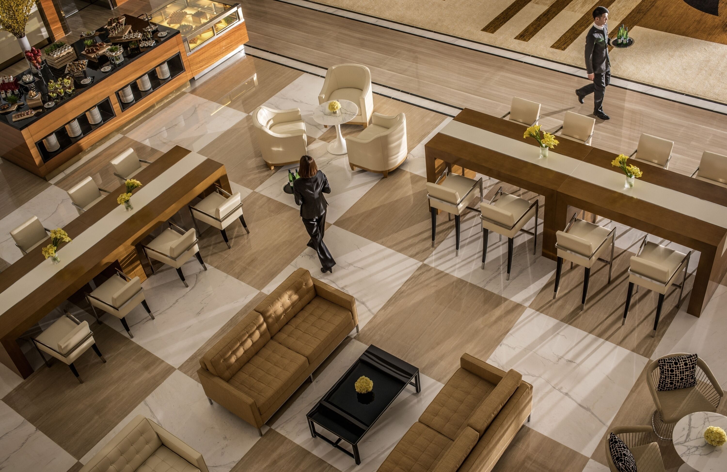 A spacious lobby with a checkered floor, multiple seating areas including sofas and chairs, a reception desk, and a display of decorative items.