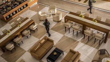 A spacious lobby with a checkered floor, multiple seating areas including sofas and chairs, a reception desk, and a display of decorative items.