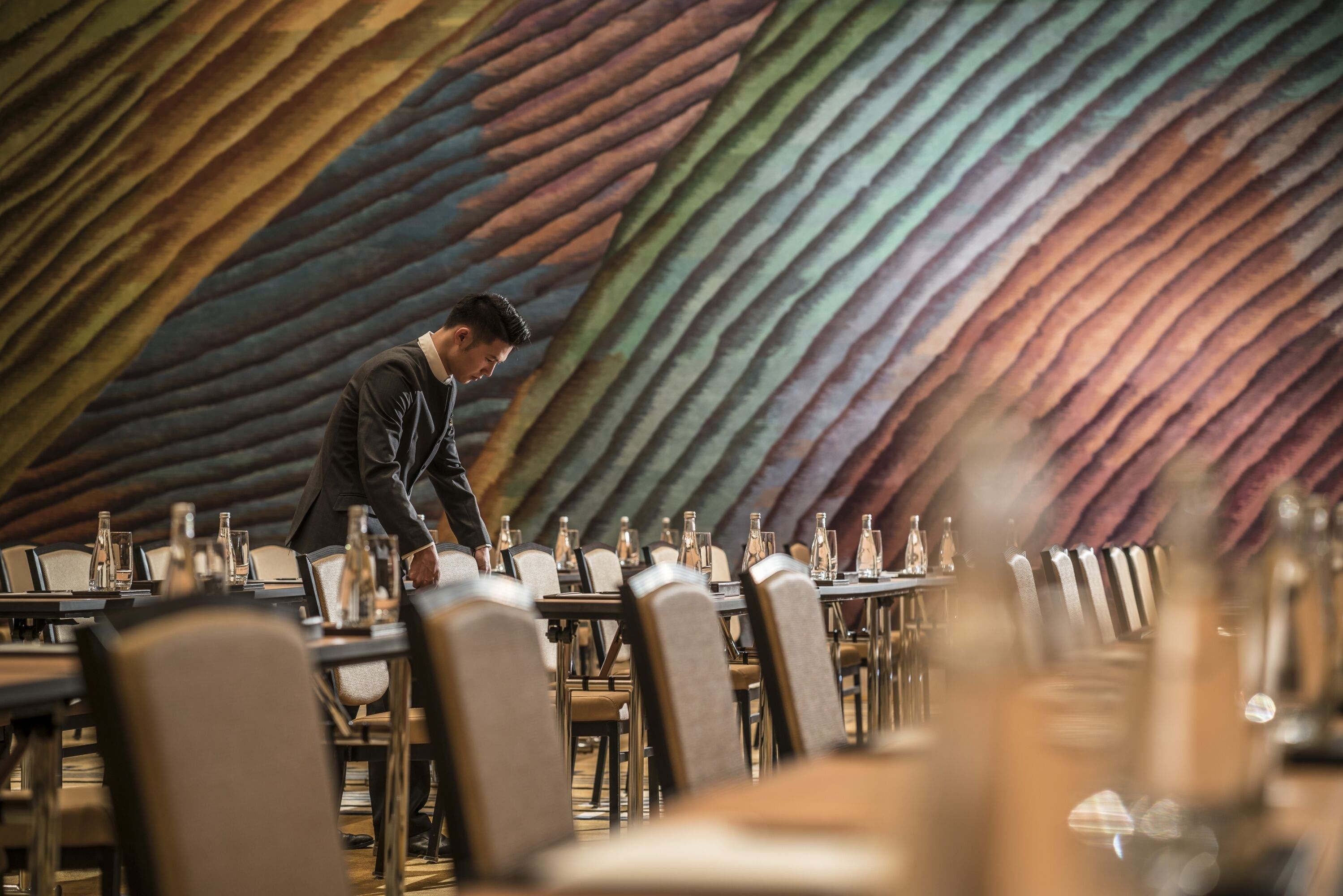 A restaurant with a modern, striped wall design and a waiter attending to a table.
