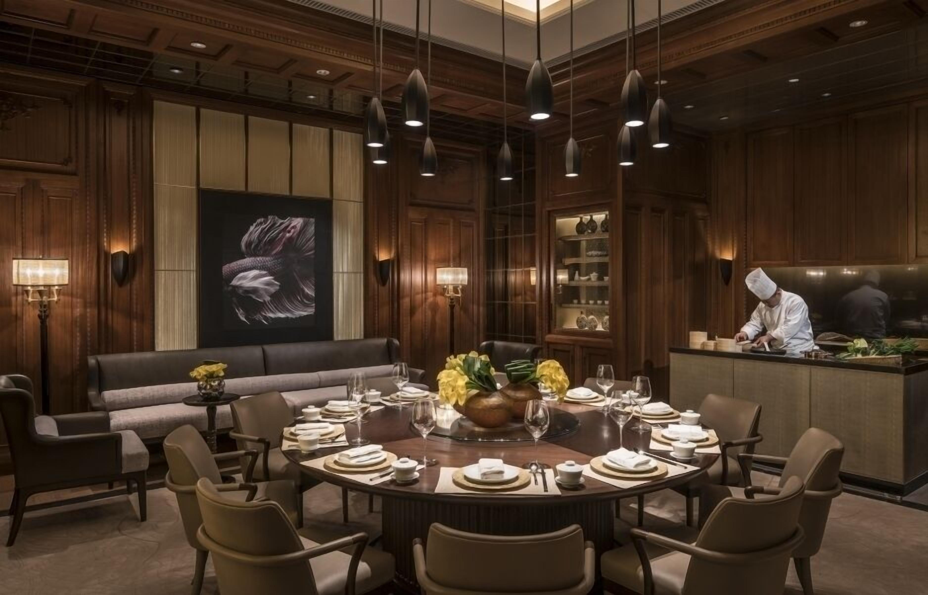 A dining area with a round table set for six, a sofa, and a chef at the counter.